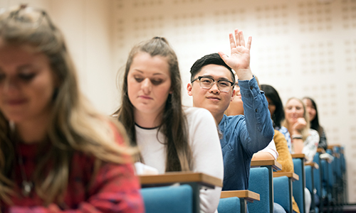 Students in lecture theatre, one with hand raised to ask a question