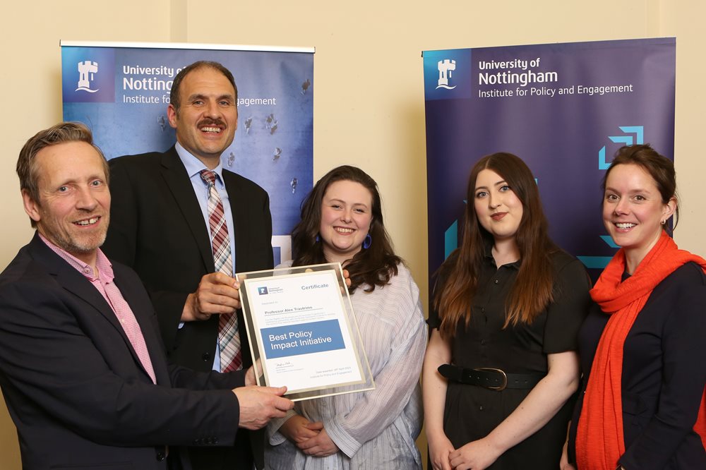 Group of five men and women holding an award certificate in front of several display banners
