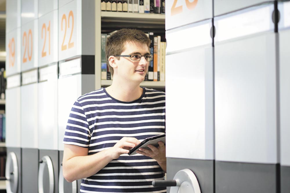 Image of a male student stood next to the library book carousels