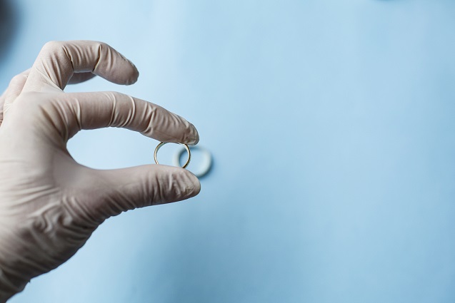 A hand wearing clinical gloves holding a wedding ring
