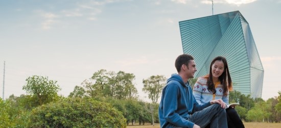 Two students sitting outside talking with trees and building behind them, Ningbo Campus