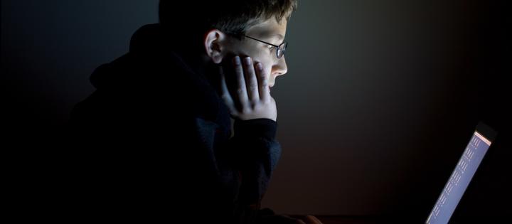 Young person looking into a laptop screen in a dark room