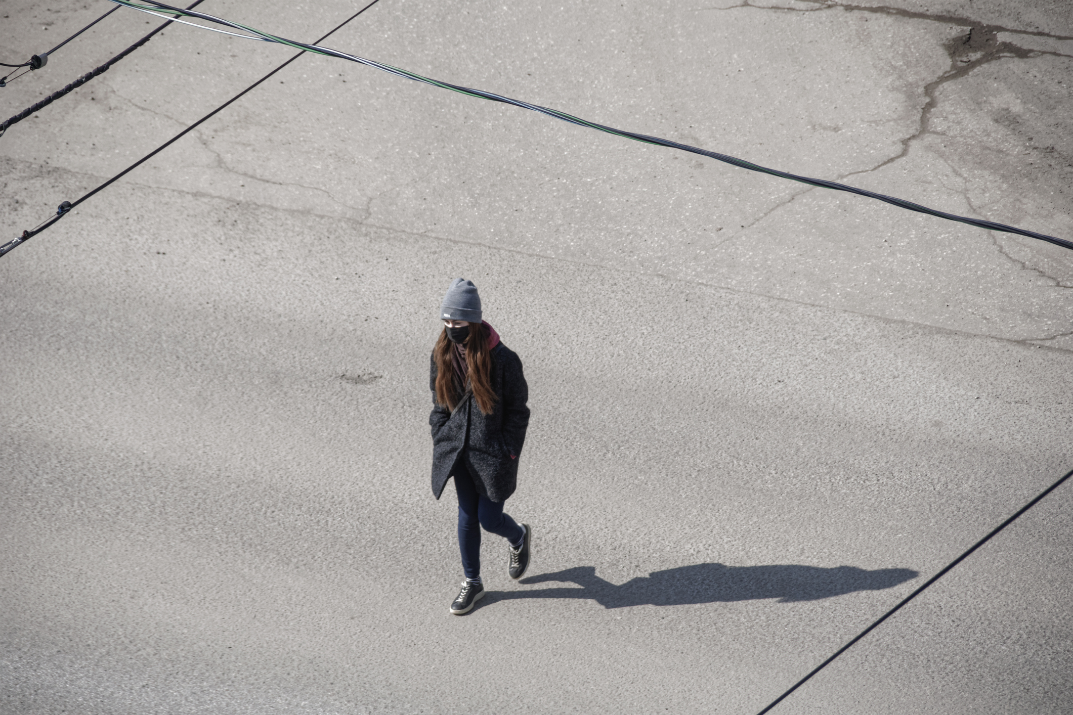 A young person walking in a winter coat and hat, wearing a mask