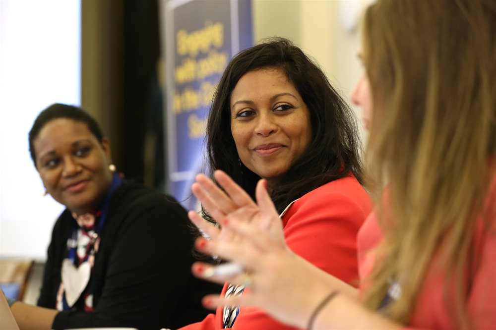 Three women lead discussion on panel in front of pop up banner