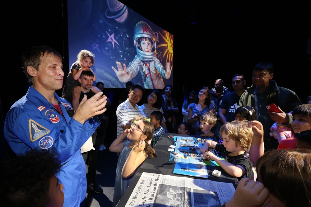Group of children crowd around a man in a boiler suit presenting a talk