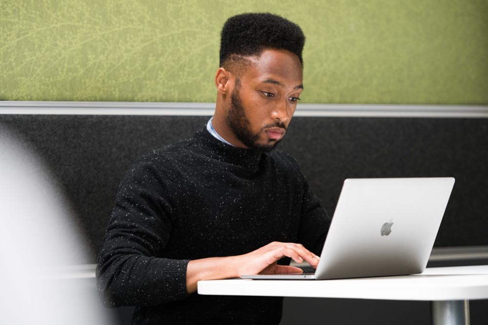 Image of a male undergraduate student sat working on a laptop in a George Green Library study booth