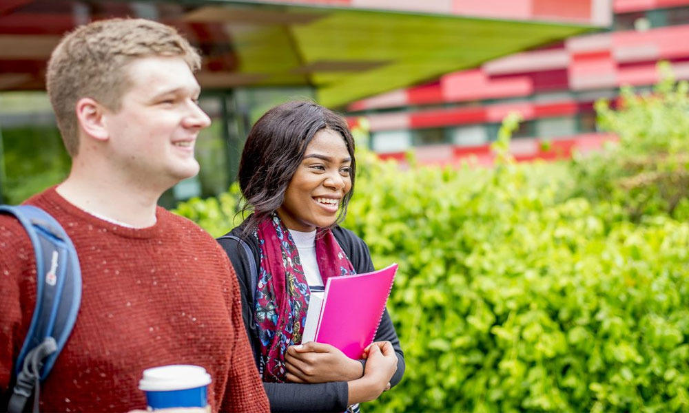 Two students walking to a lecture with folders and a coffee cup