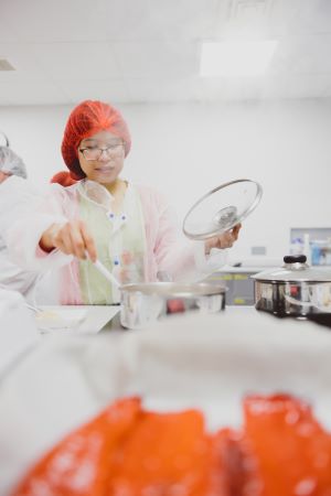 A person wearing a white coat and hairnet holdng a metallic tray