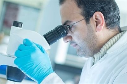 Bespectacled man in lab-wear operating a microscope