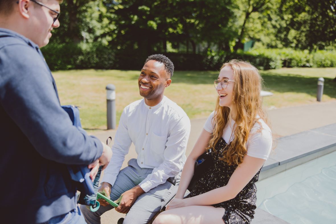 Three students sitting in sunshine talking and laughing