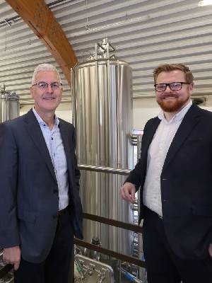 Two people standing in an outdoor setting, one of them is wearing a beekeepers outfit