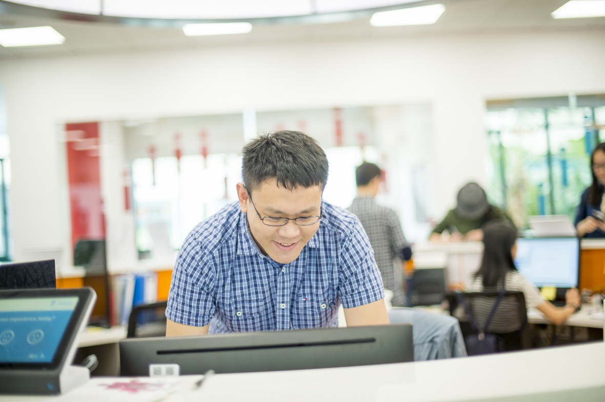 Male student wearing a blue shirt smiling at a computer screen