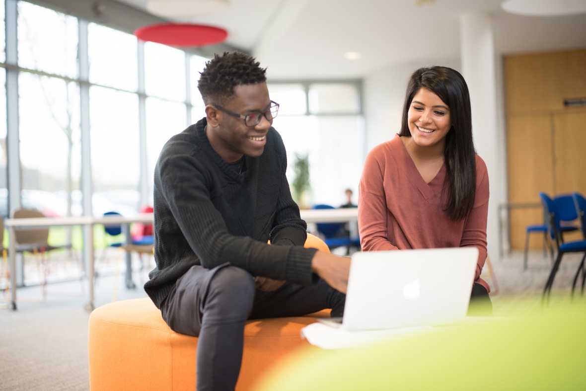 Male and female students looking at a laptop screen and smiling