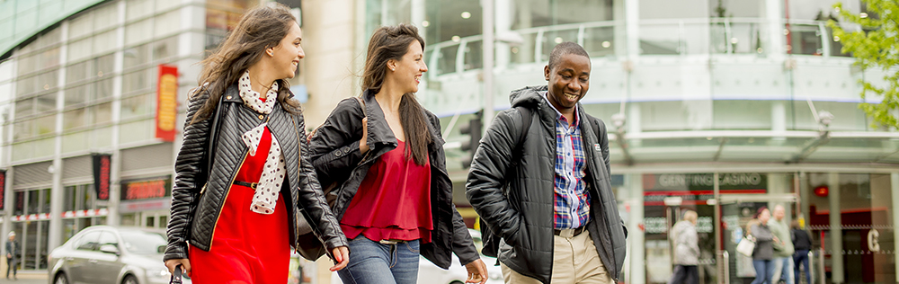Three students walking in front of a glass building