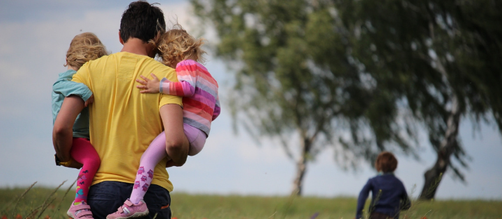 Man carrying two children walking through a field