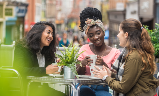 Three students sitting outside a cafe talking and smiling