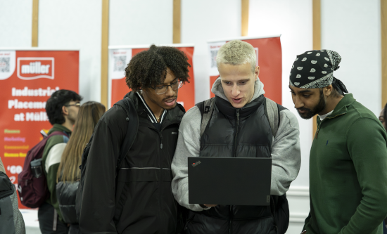 Three students gathered around laptop at recruitment fair